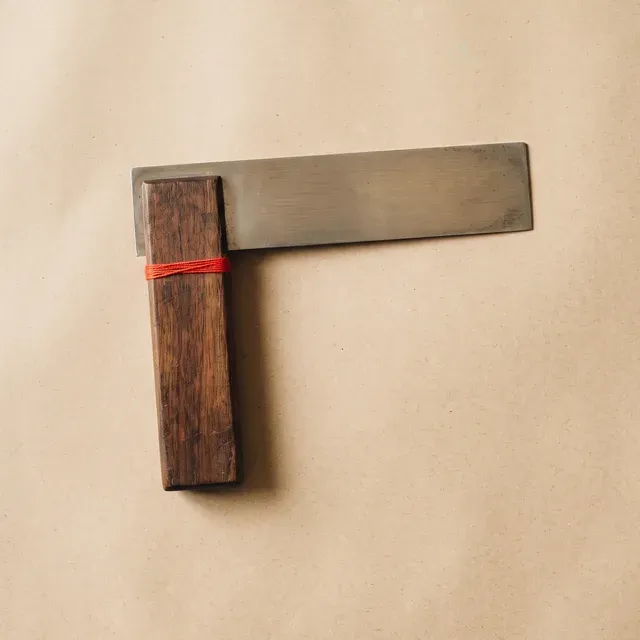 Anschlagwinkel aus Stahl und Holz auf Kraftpapier, mit einem roten Faden um den Griff